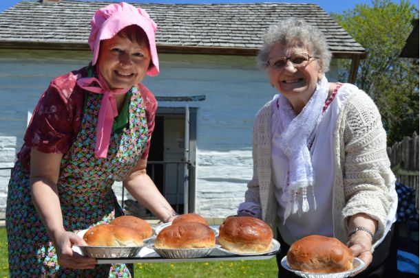 Two women holding a tray of baked bread